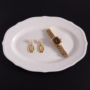 Nahaufnahme goldener Zirkonia-Ohrringe und Armbanduhr auf weißem Teller