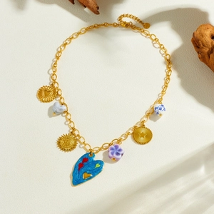 Gold stainless steel necklace with bohemian enamel heart and ceramic charms on white art surface