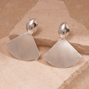 Detail of silver brushed metal fan-shaped earrings on a textured beige stone background
