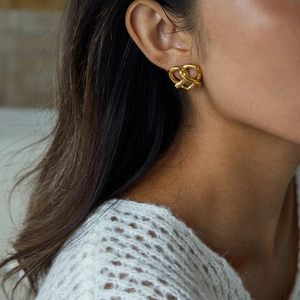 Gros plan sur une boucle d'oreille cœur noué en acier doré 18 carats portée par mannequin