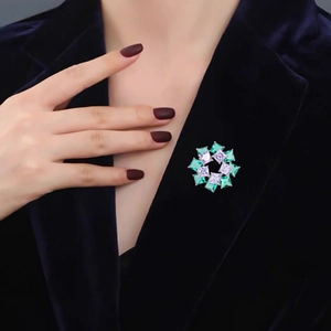 Elegant emerald and purple gemstone brooch styled on a dark blue velvet jacket