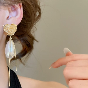 Detail of golden rose stud earrings with teardrop pearls and long golden tassel chains