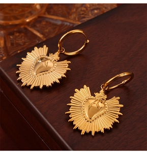 Detail of sacred heart gold earrings with radiant sunburst lines on wooden texture