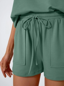 Detail of drawstring elastic waist and large patch pockets on green knit lounge shorts