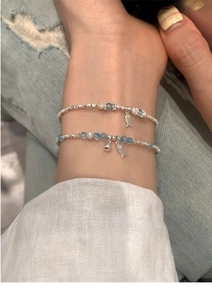 Detail of layered silver beads, blue gemstones and pearl bracelets with small fish charms