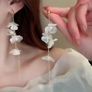 Détail de boucles d'oreilles à pompons longs avec pétales blancs et chaînes dorées
