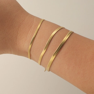Detail shot of three golden stainless steel flat snake chains on a model's wrist