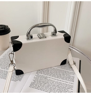 Close-up of white mini suitcase bag with black rivet corners and silver metal handle