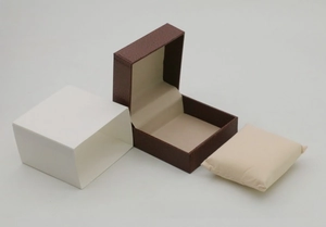 Detailed view of dark brown faux leather watch box with beige pillow and white sleeve