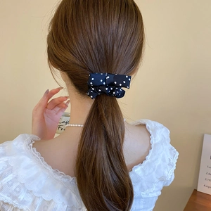 Detail of a black polka dot silk bow scrunchie styled on a elegant ponytail
