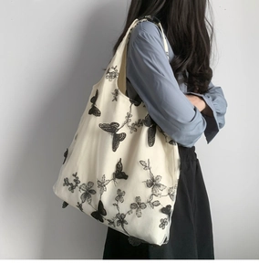 Dettaglio ricamo farfalle nere su borsa tote in tela beige indossata da una modella