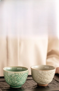 Detail of embossed dragon pattern on ceramic teacups in celadon and white finishes