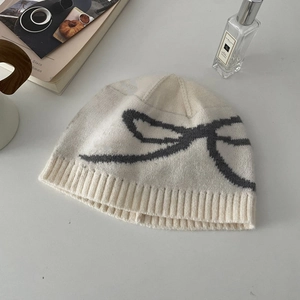 Detailed knit texture of beige winter beanie featuring grey jacquard bow pattern
