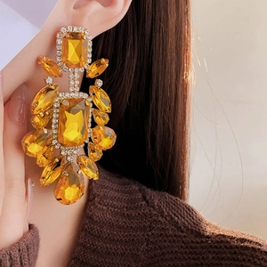 Detail of luxury gold drop earrings with amber stones and rhinestones worn by a model