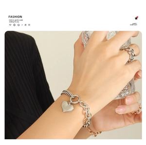 Detail of silver heart charm bracelet and chunky chain ring worn by model with water glass