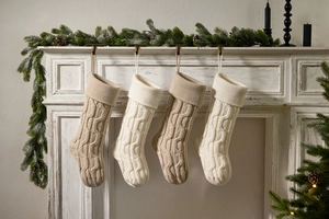 Close-up of four knitted Christmas stockings in beige and ivory on a fireplace mantle