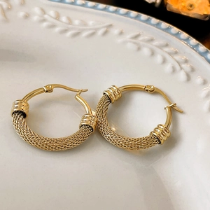 Close-up of gold woven texture hoop earrings with polished metal clasp details