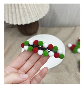 Detail of red green and white Christmas pom pom hair clip held against a cozy home background