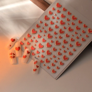 3D red heart nail sticker with golden serrated edges on white manicure background