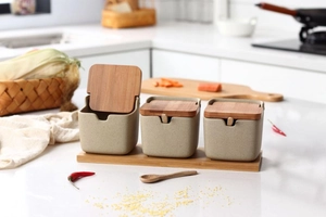 Detail of three beige ceramic seasoning jars with wooden lids and spoons on wood tray