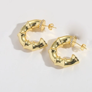 Close-up of gold C-shaped bamboo texture earrings with sparkling pavé crystal detail