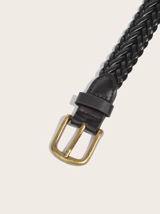 Close-up of black braided leather belt with gold metal buckle on beige background