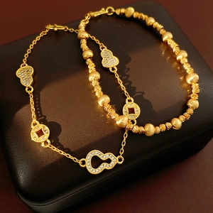 Macro shot of 24k gold plated bracelets with zircon gourd and coin charms on wood