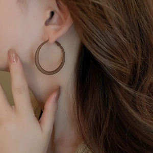 Close-up of matte brown oversized hoop earrings worn by a model with long hair
