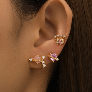 Close-up of pink heart planet and butterfly studs on ear with gold plating and crystals