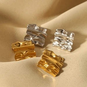 Details von quadratischen Gold- und Silberohrringen mit wellenförmiger Metallstruktur