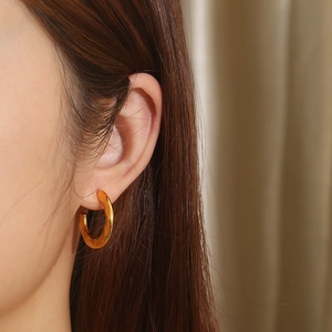 Close-up of a gold-plated C-shaped quilted hoop earring worn on a female model ear