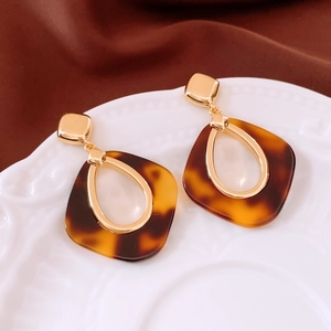 Gros plan de boucles d'oreilles en résine écaille avec accents dorés sur plateau en porcelaine
