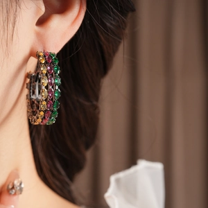Close-up of vintage gold hoop earrings with green, yellow, and fuchsia gemstones on model