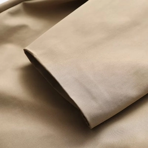 Detailansicht des khakifarbenen Trenchcoat-Stoffs mit Fokus auf Naht und feiner Textur