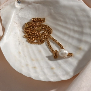 Detail of a gold Cuban chain necklace with a freshwater pearl inside a white seashell