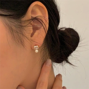 Close-up of pearl and square zircon gold earrings worn on ear showing elegant detail