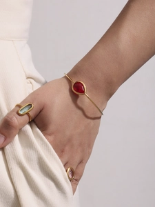 Detail of 18k gold-plated bangle with red teardrop stone and rope-textured gemstone rings