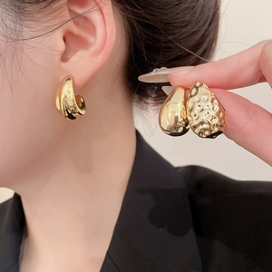 Detail of gold teardrop earrings showing smooth and hammered metal textures on a model