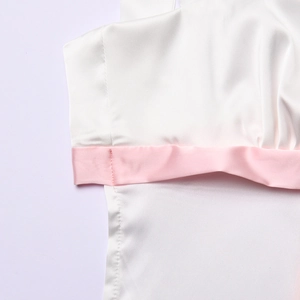 Detailaufnahme des weißen Satintops mit rosa Verzierung und glatter Stofftextur