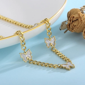 Detail of gold NK chain necklace with white shell butterfly charms on ceramic plate
