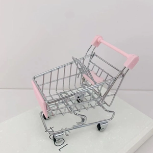 Close-up of mini metal shopping cart toy with pink plastic handles on decorative book
