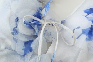 Détail d'une robe en mousseline fleurie bleue et blanche avec fleur 3D et cordon serrage