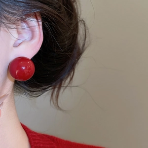 Close-up of a glossy red spherical stud earring worn with a matching red knit sweater