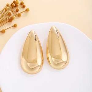 Close-up of gold drop earrings with a polished finish on a white tray with dried flowers