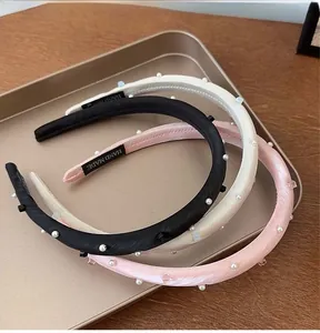 Close-up of handmade satin headbands with pearls in black, white, and pink on a gold tray