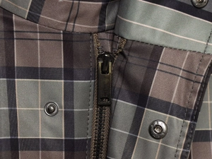 Close-up of plaid fabric texture with black metal zipper and silver snap buttons