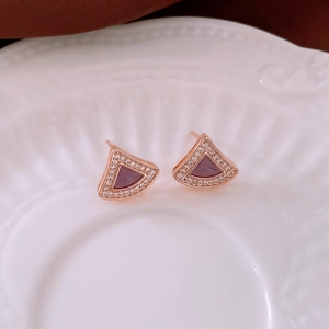Macro shot of rose gold fan-shaped stud earrings with magenta gemstone on white ceramic plate