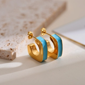Detailed shot of golden C-shaped hoop earrings with sky blue enamel on a stone surface