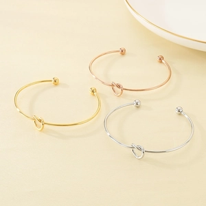 Detailed view of three minimalist knotted C-shape bracelets in gold, silver, and rose gold
