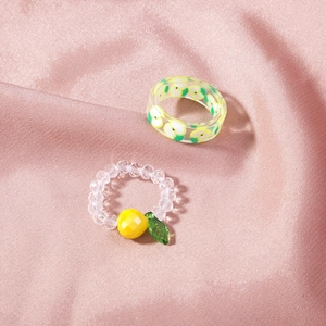 Detail of transparent resin rings with apple patterns and yellow lemon charm on silk